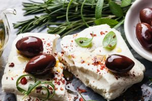 Feta cheese with olives and green herbs on gray marble background