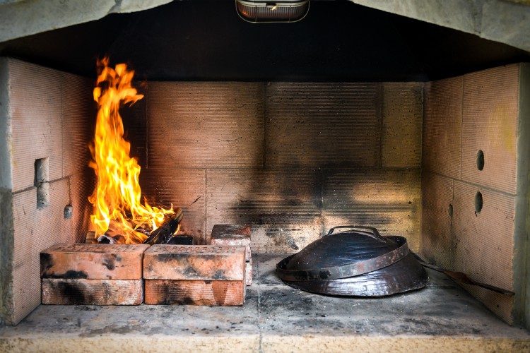 Cooking of traditional Balkan Greek Mediterranean Croatian meal Peka in metal pots called sac sach or sache or a metal lid. Fireplace with open fire and burning coals.