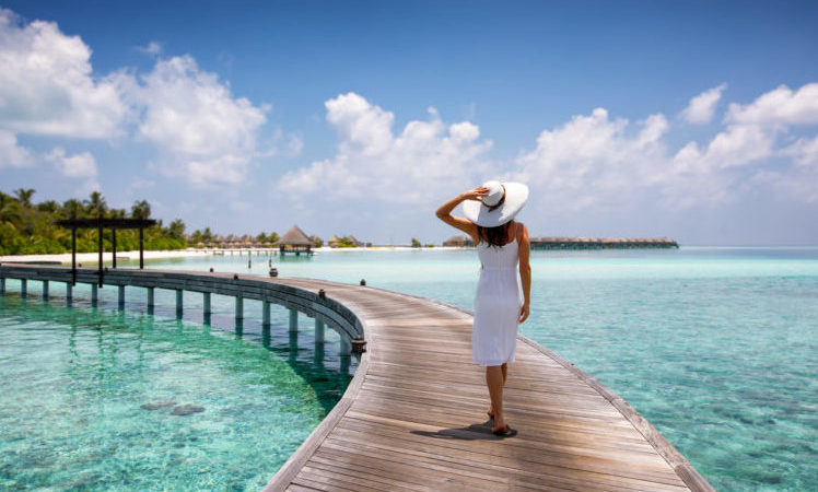 Woman walks on a wooden jetty towards a tropical island in the Maldives