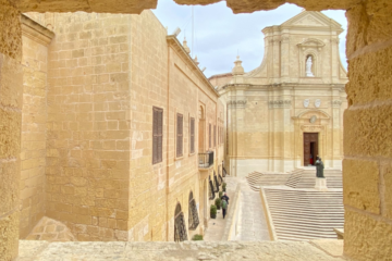 one of the things to do in Gozo: an image of the cathedral through a rocky window