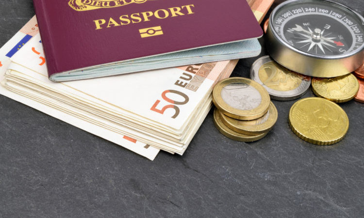 An arrangement of Euro notes, coins, passport and compass on slate.